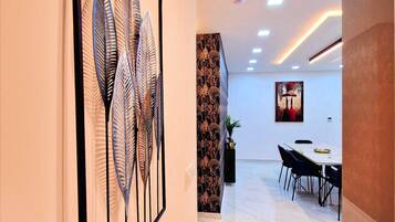 A modern interior with a dining area, a wall-mounted art piece, and a ceiling with recessed lighting.