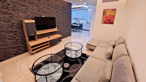 A modern living room with a flat-screen TV, a sofa, a coffee table, and a patterned rug. - Sveltos Residence 3Bedroom Suites (Larnaca)