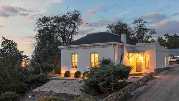 A two-story house with a stone foundation, a sloped roof, and a well-maintained garden with various shrubs and a small pond. - The Cottage-Historical Home Valley Views! (S) (Ogden)