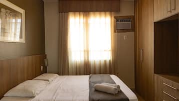 A hotel room with a bed, wooden wardrobe, and a window with curtains.