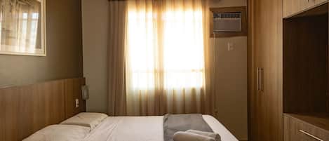 A hotel room with a bed, wooden wardrobe, and a window with curtains.