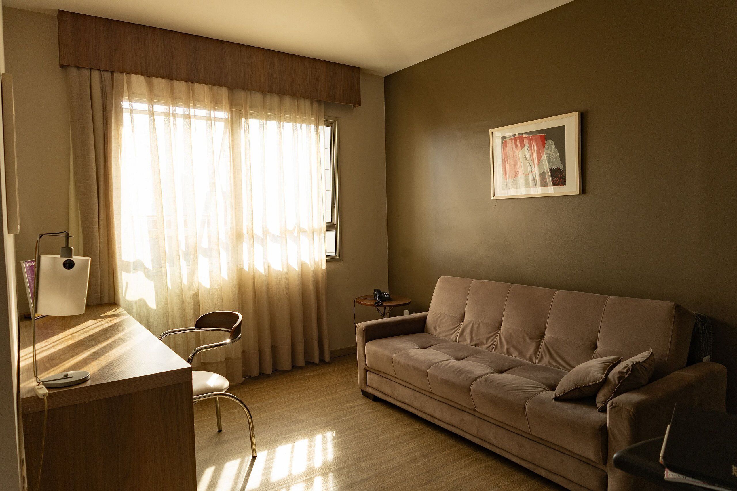A living room with a sofa, a chair, a desk with a lamp, and a small table with a phone.