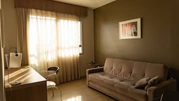 Una sala de estar con sofá, sillón, escritorio con lámpara y una pequeña mesa con teléfono.