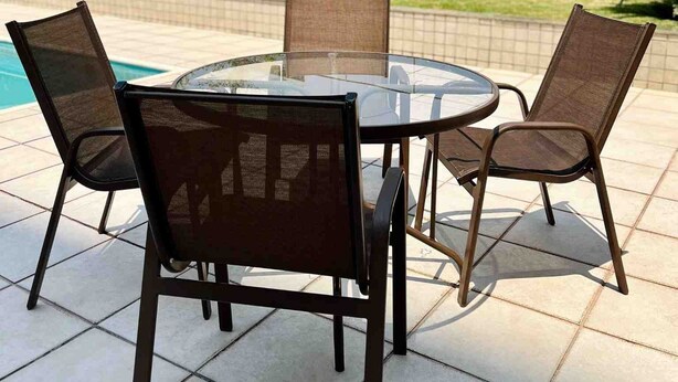 Un espace extérieur aménagé avec une table ronde en verre et quatre chaises, entouré d’une terrasse carrelée.
