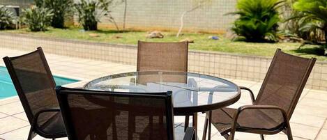 An outdoor seating area with a round glass table and four chairs, surrounded by a tiled patio.