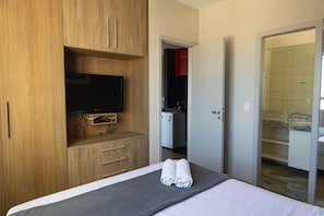 Habitación de hotel con cama, televisor, armario de madera y baño visible a través de una puerta abierta.