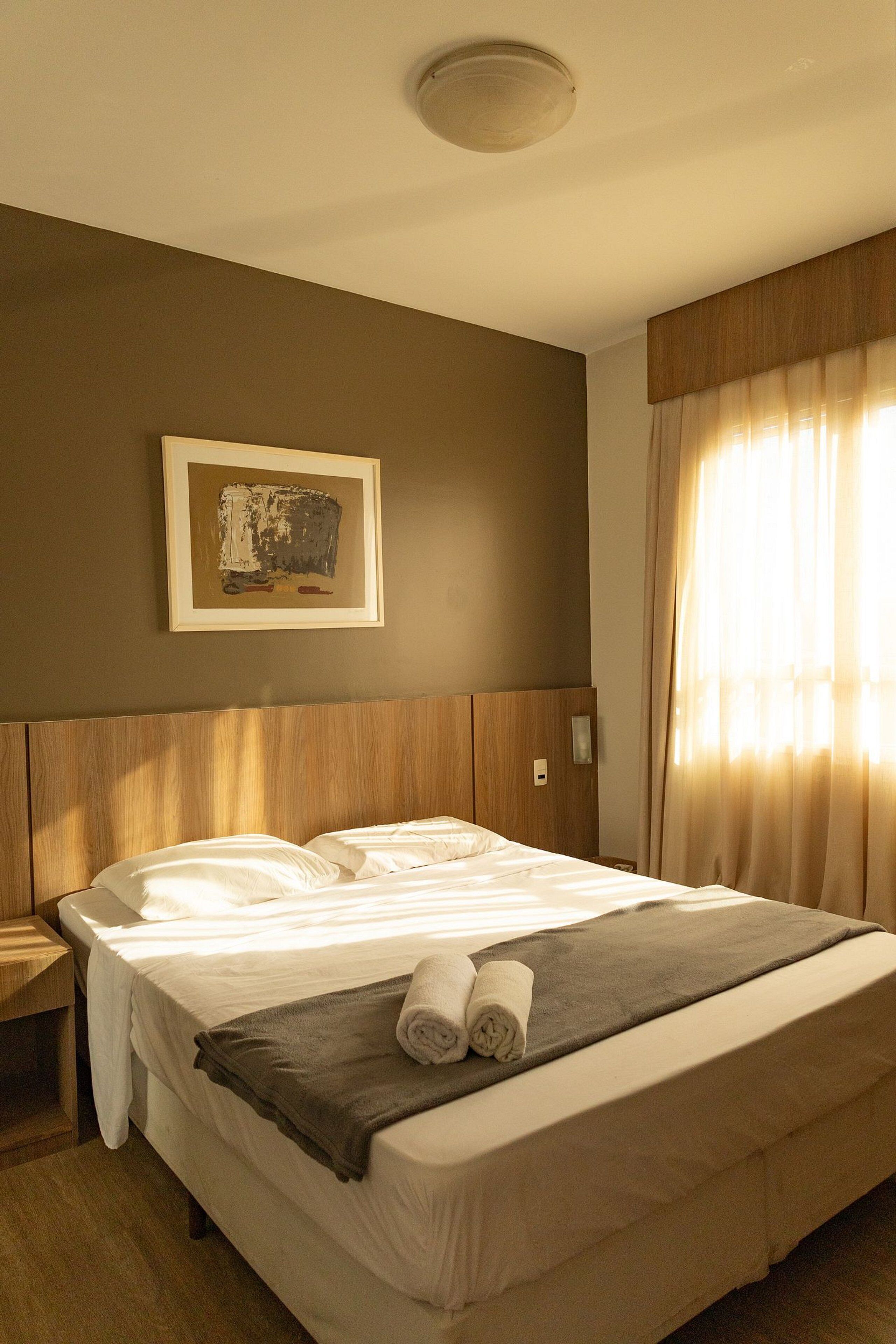 Habitación de hotel con una cama grande, una mesita de noche, un cuadro enmarcado en la pared y una ventana con cortinas.