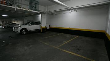 Un aparcamiento con varios coches estacionados, suelo de hormigón y líneas pintadas en amarillo y negro.