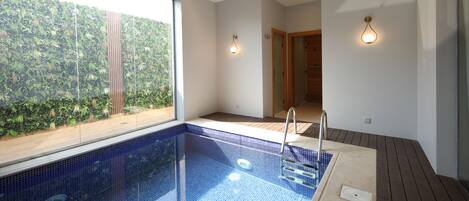 A modern indoor swimming pool with a clear view of the surrounding greenery through large windows.