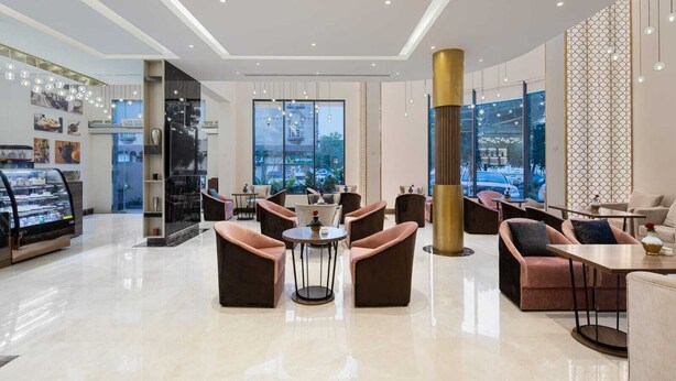 A modern hotel lobby with a central seating area, large windows, and a dessert display. - Gladiolus Hotel (Jeddah)