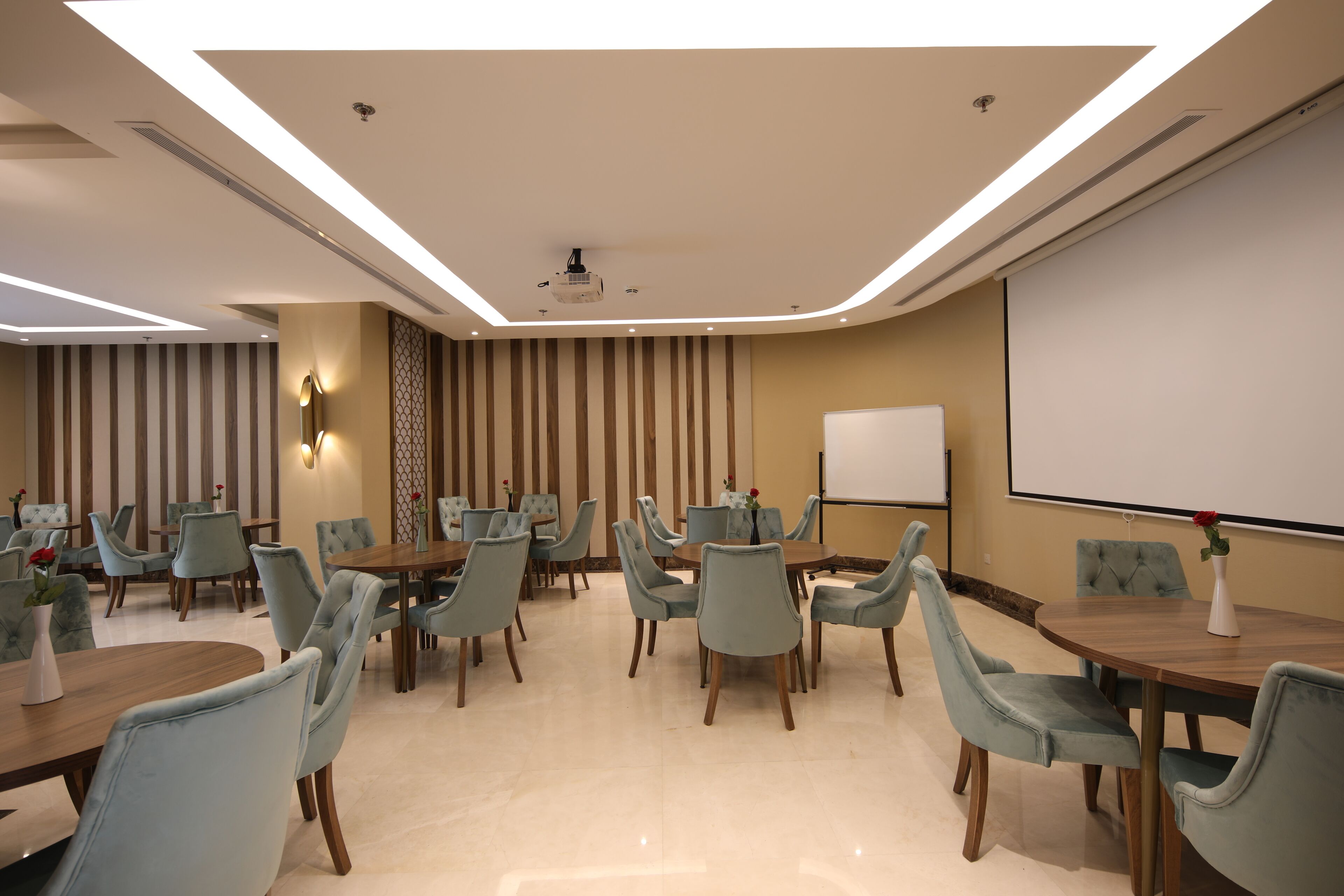 A conference room with a projector screen, multiple tables, and chairs.