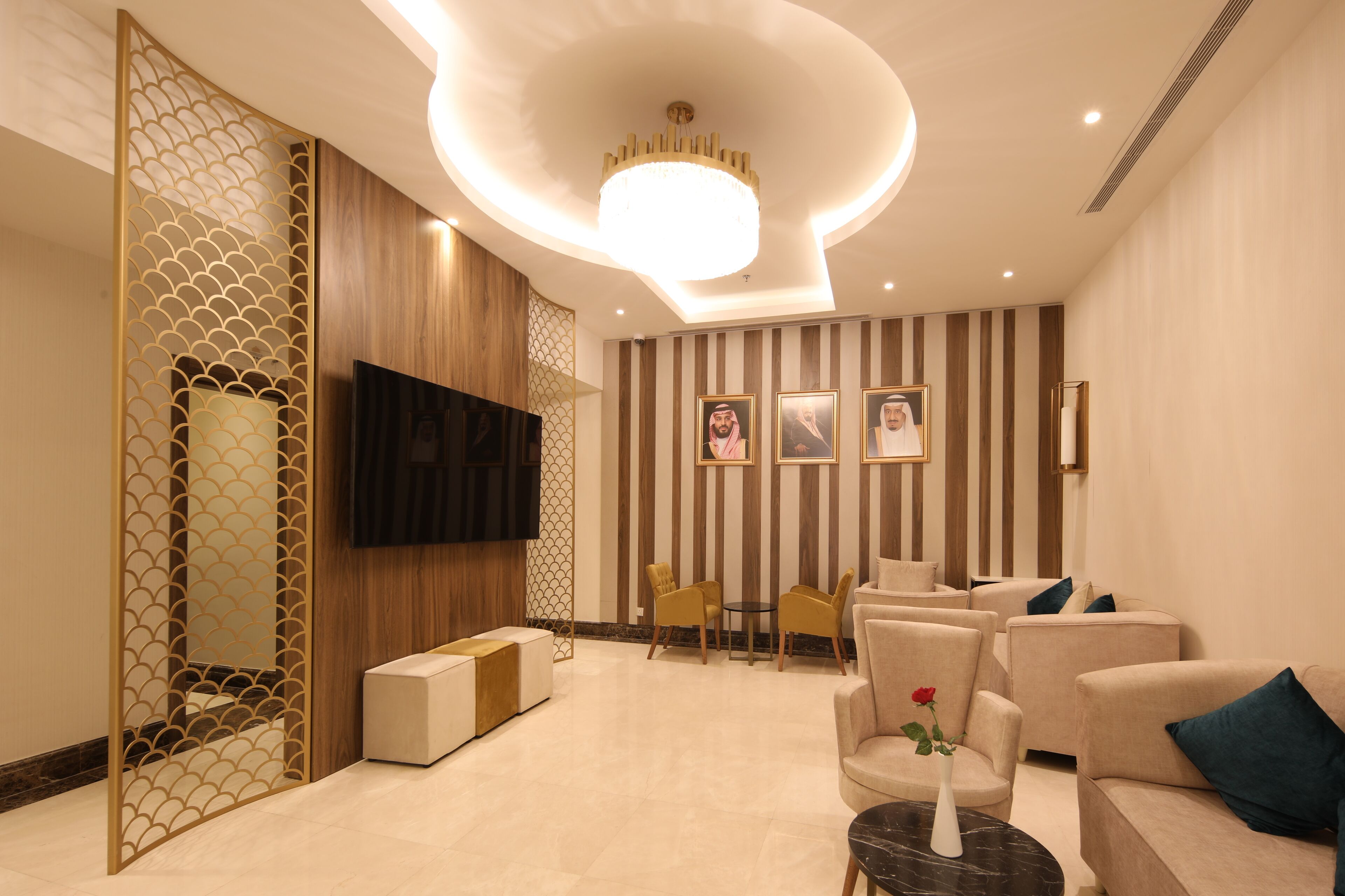 A modern living room with a flat-screen TV, comfortable seating, a decorative wall, and a chandelier.