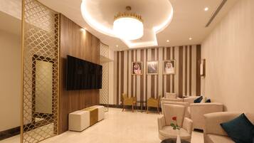 A modern living room with a flat-screen TV, comfortable seating, a decorative wall, and a chandelier.