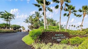 Waikoloa Colony Villas -nimelle varustettu opaste, jonka vieressä on asfaltoitu tie ja palmuja.