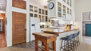 A kitchen with wooden cabinetry, a wooden island with stools, and a clock on the wall.