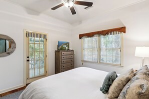 Un dormitorio con cama, cómoda, ventilador de techo y dos ventanas con persianas.