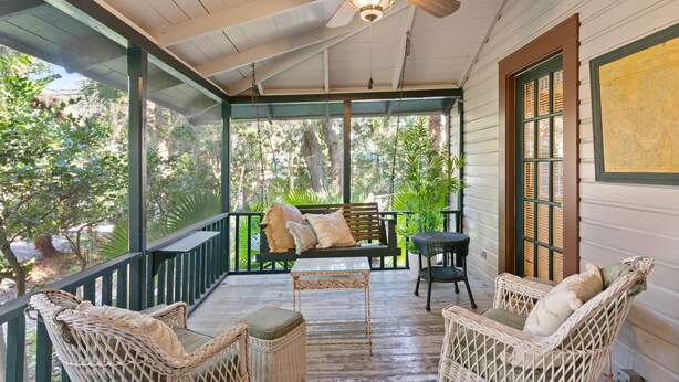 A covered porch with wicker furniture, a ceiling fan, and a view of the surrounding greenery.