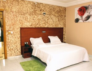 A hotel room with a wooden headboard, a green rug, and a painting of a rose on the wall. - Alicia Hotel (Douala)