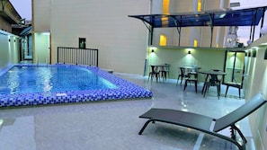 A swimming pool with a tiled edge, surrounded by a covered seating area with tables and chairs. - Alicia Hotel (Douala)