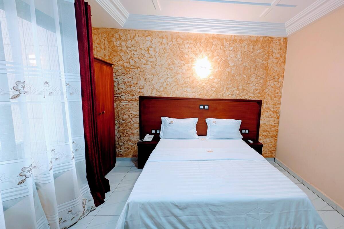 A hotel room with a large bed, a wooden headboard, a nightstand with a phone, and a wall with a textured pattern.