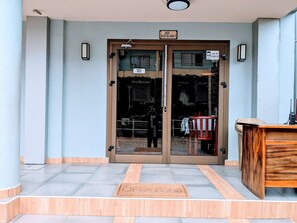 A hotel entrance with a glass door, a wooden reception desk, and a tiled floor. - Alicia Hotel (Douala)