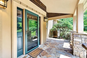 A covered porch with a stone floor, a door with a glass panel, and a welcome mat.