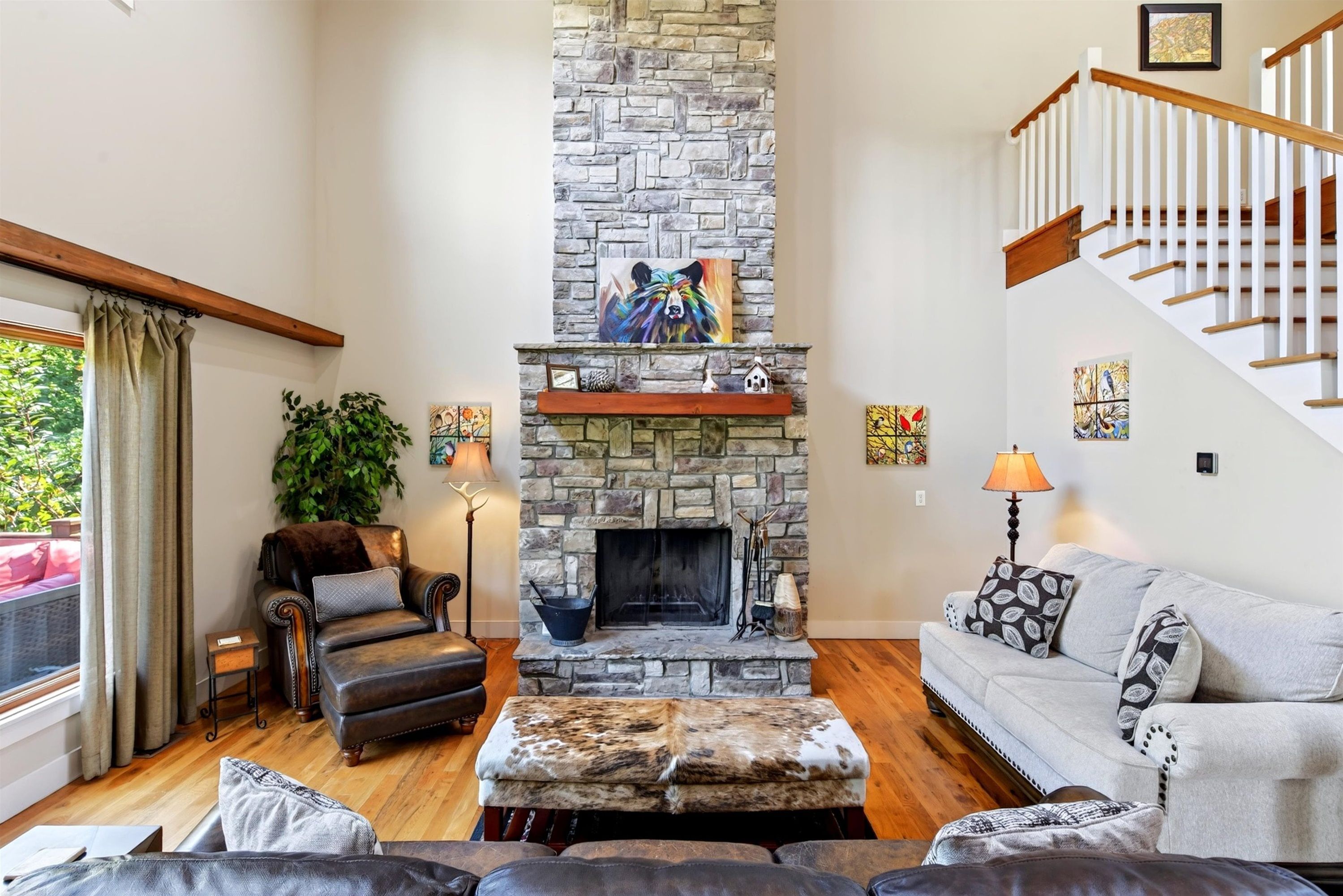 A living room with a stone fireplace, leather furniture, a staircase, and artwork on the walls.