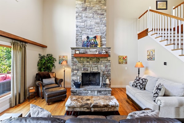 A living room with a stone fireplace, leather furniture, a staircase, and artwork on the walls.