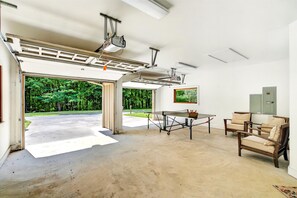 Un vaste espace intérieur doté d’un sol en béton, d’une table avec des chaises et offrant une vue sur un paysage verdoyant par une porte ouverte.