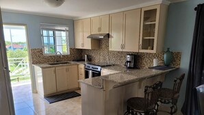 A kitchen with beige cabinets, a stove, a coffee maker, and two chairs. - Soleil de la Palms (St. Ann's Bay)