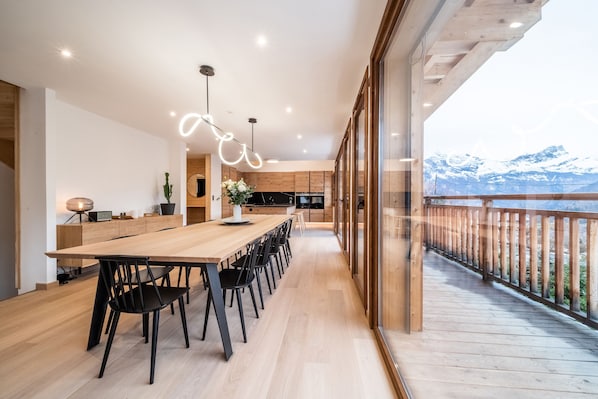 Une cuisine moderne avec une table et des chaises en bois, une grande fenêtre et une vue sur les montagnes.
