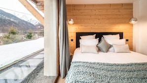 Una camera da letto con soffitto in legno, un letto con biancheria bianca e vista su un paesaggio innevato.