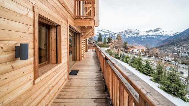 Una baita di legno con un balcone affacciato su una catena montuosa innevata.