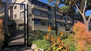 Un edificio moderno con entrada protegida por un portón, rodeado de jardines ajardinados y árboles.