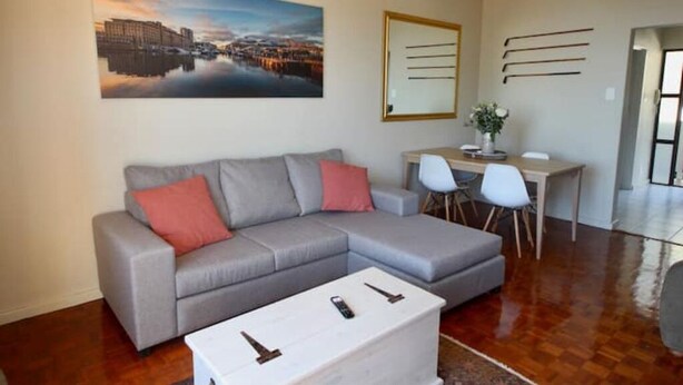 Una sala de estar moderna con un sofá seccional gris, una mesa de centro blanca y un cuadro con una vista urbana en la pared.