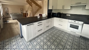 A modern kitchen with white cabinets, black countertops, and patterned floor tiles. - Gîte Les Roches D'Étigues near Etretat (Vattetot-sur-Mer)