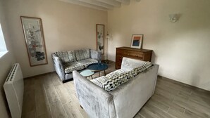 A living room with a sofa, a small table, a dresser, and a radiator. - Gîte Les Roches D'Étigues near Etretat (Vattetot-sur-Mer)
