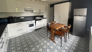 A compact kitchen with white cabinets, a black countertop, a dining table with chairs, and a patterned floor. - Gîte Les Roches D'Étigues near Etretat (Vattetot-sur-Mer)