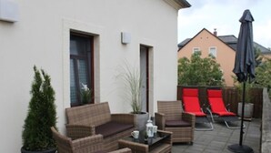 Ein möblierter Patio-Bereich im Freien mit Korbmöbeln, einem kleinen Tisch und einem Blumentopf.