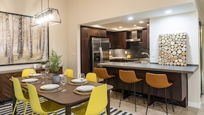 A modern kitchen with a central island, stainless steel appliances, and a dining area with yellow chairs and a dark wooden table. - Washington State Inspired, Free Parking (Bellevue)