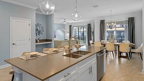 A modern kitchen with a central island, a dining area with a chandelier, and a view of the outside. - 🍂 Fall Special! Bliss Pool Villa Close to Disney & Universal; Great Clubhouse🏝️ (Kissimmee)