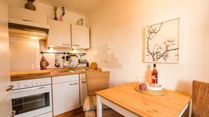 Una cocina compacta con armarios blancos, una encimera de madera y una mesa de comedor con una silla de mimbre.