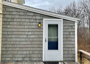 Ein Haus mit weißer Tür, einer kleinen Veranda und einem Laternen an der Wand.