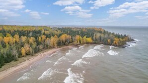 Eine Küstenlandschaft mit Sandstrand und bewaldetem Gebiet mit herbstlich gefärbten Bäumen.