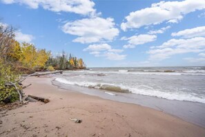 A beach with a sandy shore, waves, and trees with autumn foliage. - Entire Home Near Lake Superior (Port Wing)