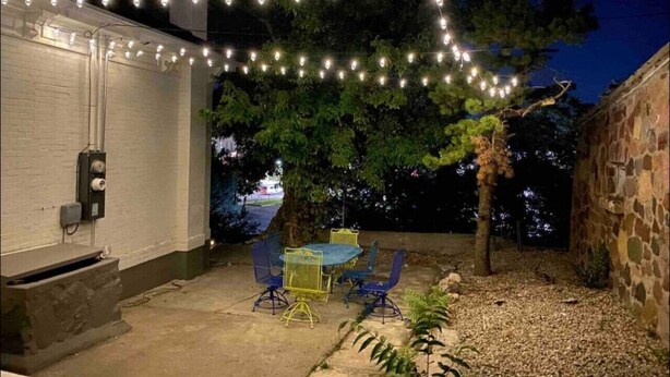 Ein Garten mit einer Terrassentisch- und Stuhlgruppe, Lichterketten und einem Baum.