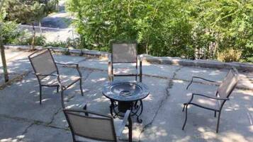 Ein Terrassenbereich im Freien mit einem runden Tisch und vier Stühlen, umgeben von Bäumen und Blick auf einen Parkplatz.