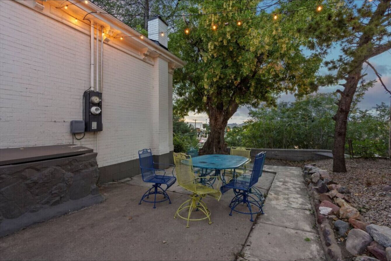An outdoor patio with a table and chairs, a white building, and a tree.