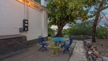 An outdoor patio with a table and chairs, a white building, and a tree.