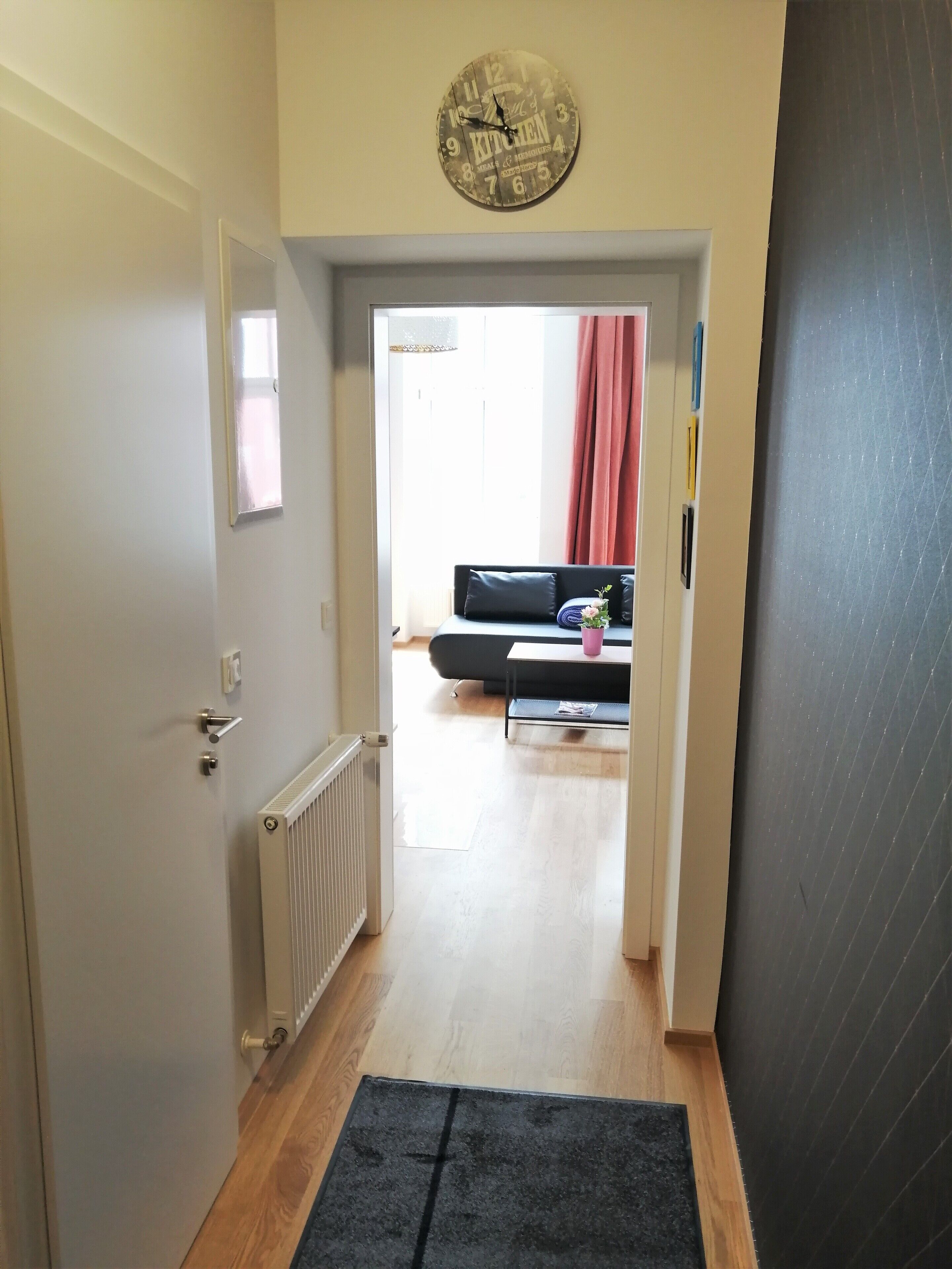 A hallway with a radiator, a black rug, and a clock on the wall.